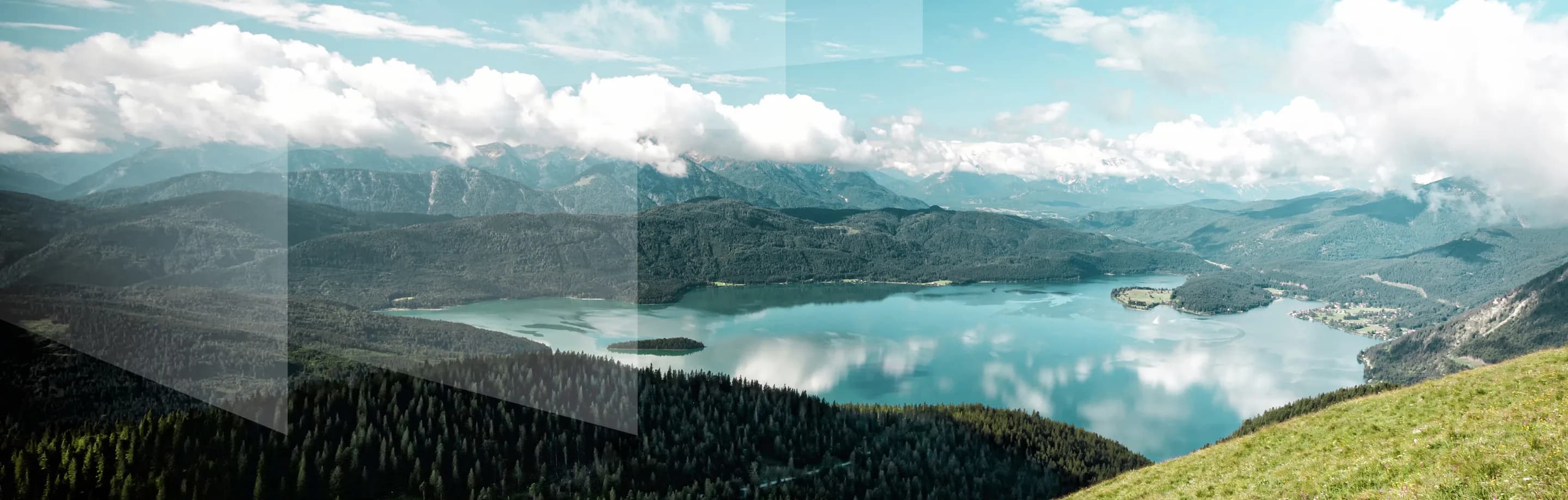 Panoramablick auf einen See umgeben von Bergen, mit Wolken am Himmel und einem grünen Hügel im Vordergrund.