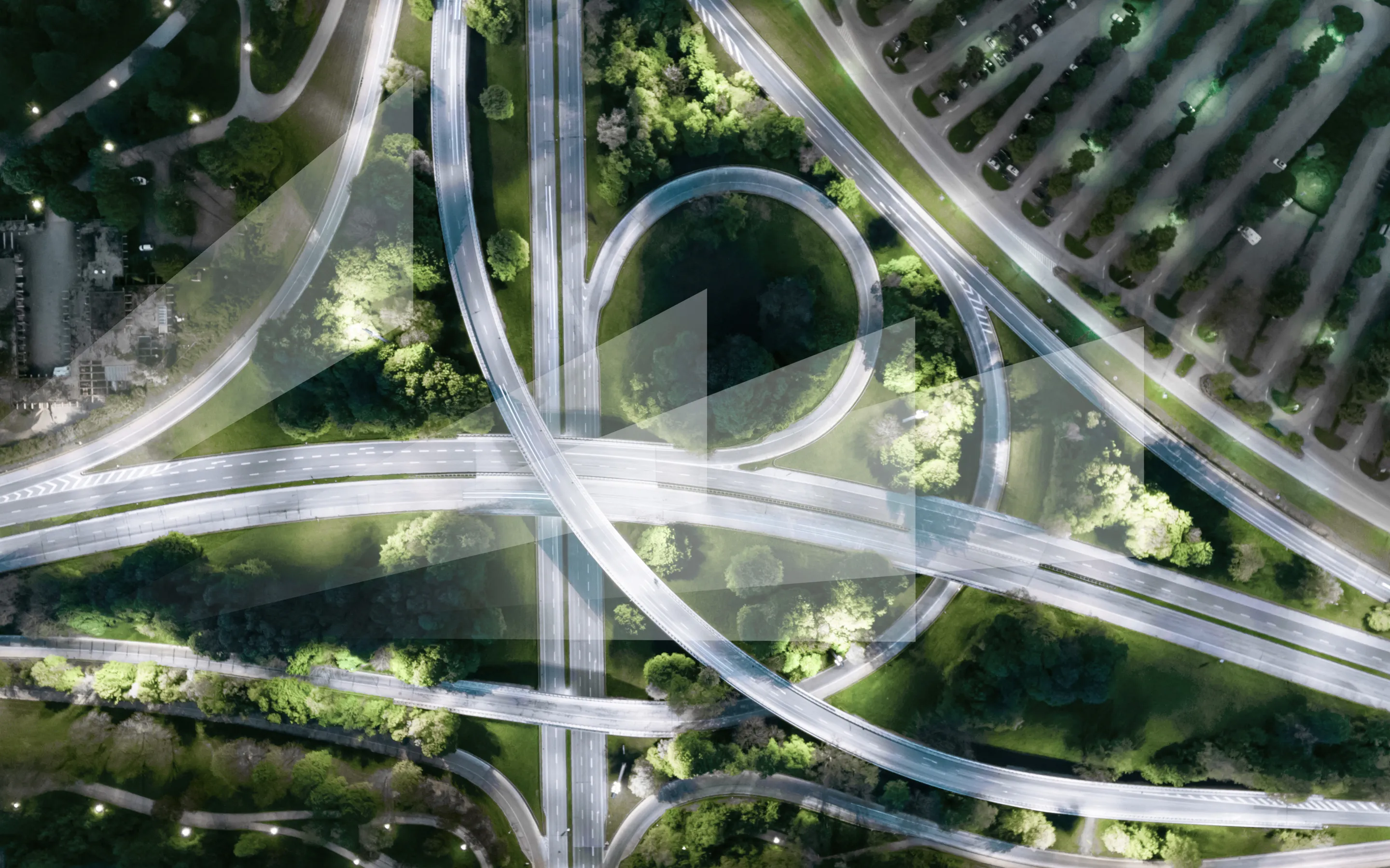 Luftaufnahme eines komplexen Autobahnkreuzes, umgeben von Bäumen und Grünflächen, bei Dämmerung.